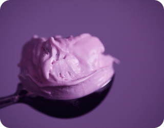 fotografia de uma bola de sorvete roxa repousando em uma colher com fundo roxo